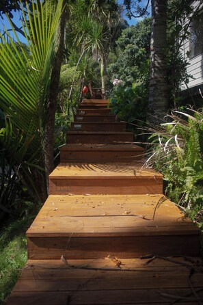 Eine Holztreppe führt einen Hügel hinauf, umgeben von üppigem Grün und Bäumen.