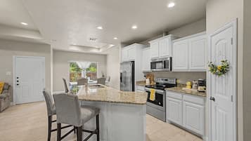 Una cocina con armarios blancos, encimera de granito, electrodomésticos de acero inoxidable y un comedor con taburete de bar.