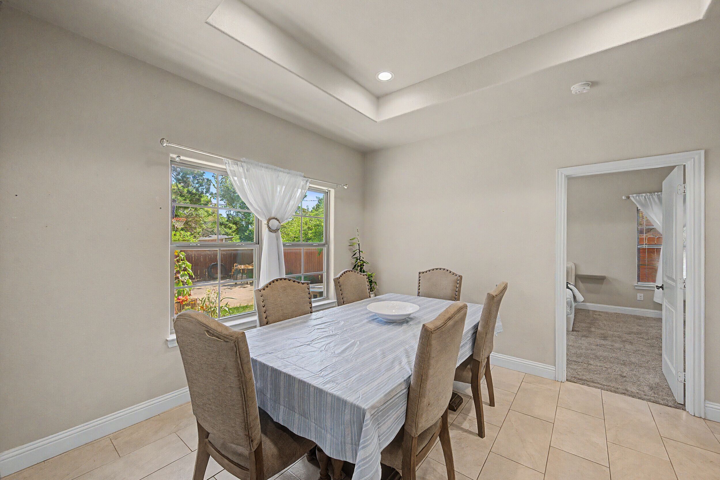 Un comedor con una mesa y sillas, una ventana con cortinas y una puerta que da a otra habitación.
