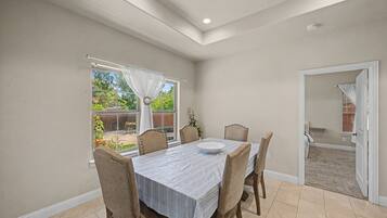 Un comedor con una mesa y sillas, una ventana con cortinas y una puerta que da a otra habitación.