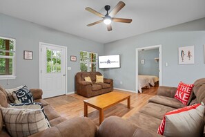 A living room with a brown sofa, a wooden coffee table, a ceiling fan, and a door leading to a bedroom. - Steps to Table Rock Lake & Port of Kimberling_Free Attraction Tickets (Kimberling City)