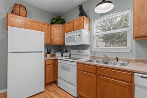 Eine Küche mit Holzausstattung, einem weißen Kühlschrank, einer Mikrowelle, einem Backofen, einem Spülbecken und einem Fenster mit Jalousien.