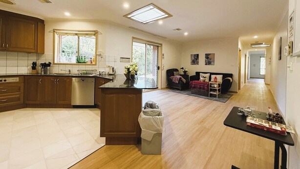 A modern kitchen with wooden cabinets, a central island, and a dining area with a sofa and table. - Cozy Queen Room Near ANU and City Centre | Parking (Turner)
