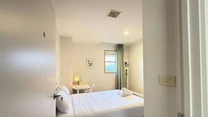 A hotel room with a bed, bedside table, lamp, window with curtains, and a small table with a lamp. - Cozy Queen Room Near ANU and City Centre | Parking (Turner)