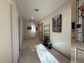 En hall med en dörr, en papperskorg, ett metallställ och en tavla på väggen.