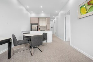 Une cuisine moderne dotée d’un îlot central, un coin repas avec une table ronde et quatre chaises, et un couloir menant à une porte.