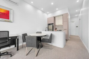 Eine moderne Küche mit einer zentralen Kochinsel, ein Essbereich mit rundem Tisch und Stühlen, und ein kleiner Arbeitsbereich mit Schreibtisch und Stuhl.