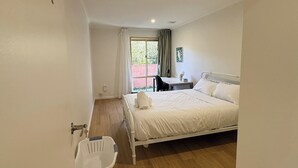 Une chambre à coucher comprenant un lit, un bureau, une chaise, une fenêtre avec des rideaux et une petite table avec une lampe.