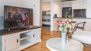 Een moderne woonkamer met een televisie, een ronde witte tafel en een bloevas.