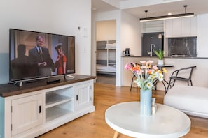 Ein modernes Wohnzimmer mit Fernseher, einem runden weißen Tisch und einer Blumenvase.