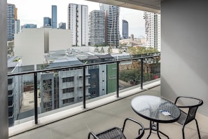 Een balkon met glazen hekwerk, een ronde tafel en twee stoelen.