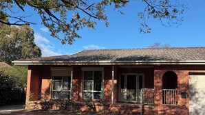 A single-story brick house with a front porch, a garage, and a clear blue sky.