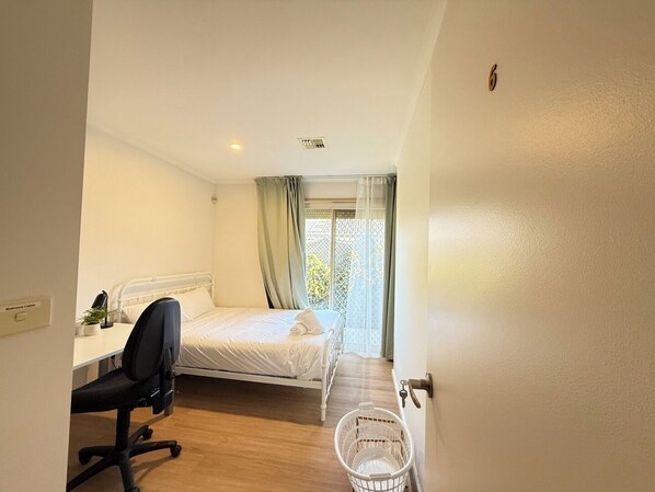 Ein Schlafzimmer mit einem Bett, einem Schreibtisch, einem Stuhl, einem Fenster mit Vorhängen und einer Tür.