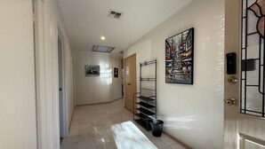 A hallway with a door, a trash bin, a metal rack, and a painting on the wall.