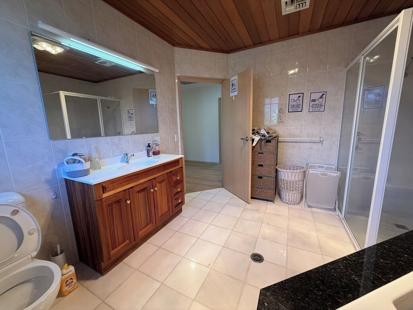 A modern bathroom with a wooden vanity, a large mirror, a shower with a glass door, and a tiled floor.