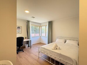A bedroom with a bed, a desk, a chair, a window, and a small plant.