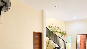 Un hall d’entrée comprenant un ensemble de canapés, une table basse, un ventilateur, un escalier et une porte portant un numéro.