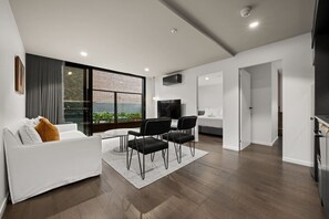 Ein modernes Wohnzimmer mit einem weißen Sofa, schwarzen Sesseln, einem Fernseher und einem großen Fenster mit Blick auf Grünflächen.