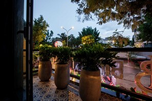 A balcony with potted plants, a view of a street with a roundabout, and a building in the background. - Bin Bin Hotel 1 - Near RMIT Univerisity (Ho Chi Minh City)
