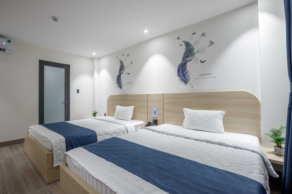 Ein Hotelzimmer mit zwei Betten, einem Holzkopfteil, Wandgemälde und einer Tür.