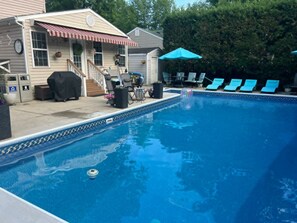 A swimming pool with a tiled edge, a covered patio with outdoor furniture, and a blue umbrella. - Cozy studio apartment near Mount Vernon with resort style yard (Alexandria)