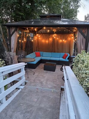An outdoor seating area with a blue sofa, a fan, and string lights. - Cozy studio apartment near Mount Vernon with resort style yard (Alexandria)