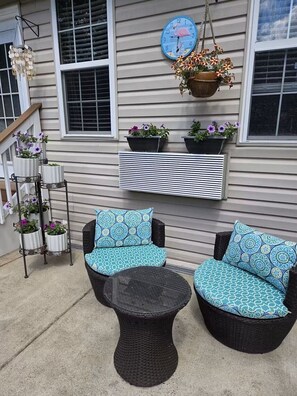 A patio with wicker furniture, a hanging flower pot, and potted plants against a house exterior. - Cozy studio apartment near Mount Vernon with resort style yard (Alexandria)