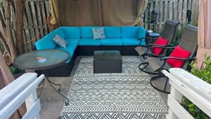 Een overdekt terras met een blauwe bank, een klein rond tafeltje en twee stoelen.