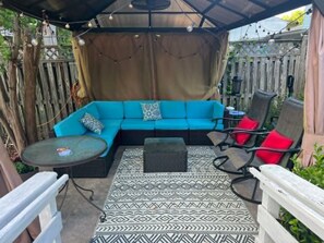 A covered patio area with a blue sofa, a small round table, and two chairs. - Cozy studio apartment near Mount Vernon with resort style yard (Alexandria)