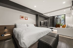 Ein modernes Hotelzimmer mit einem großen Bett, Nachttisch und einer Sitzecke mit Sofa und Sessel.