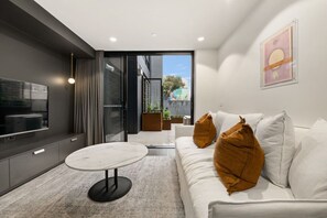 Ein modernes Wohnzimmer mit einer Couch, einem Couchtisch, einem Fernseher und einer Schiebetür zu einem Außenbereich.
