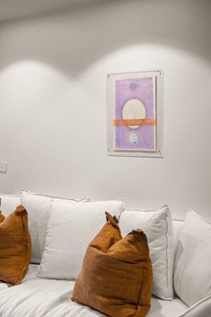 Ein Zimmer mit einem weißen Bett, einem gerahmten abstrakten Gemälde und einer weißen Wand.