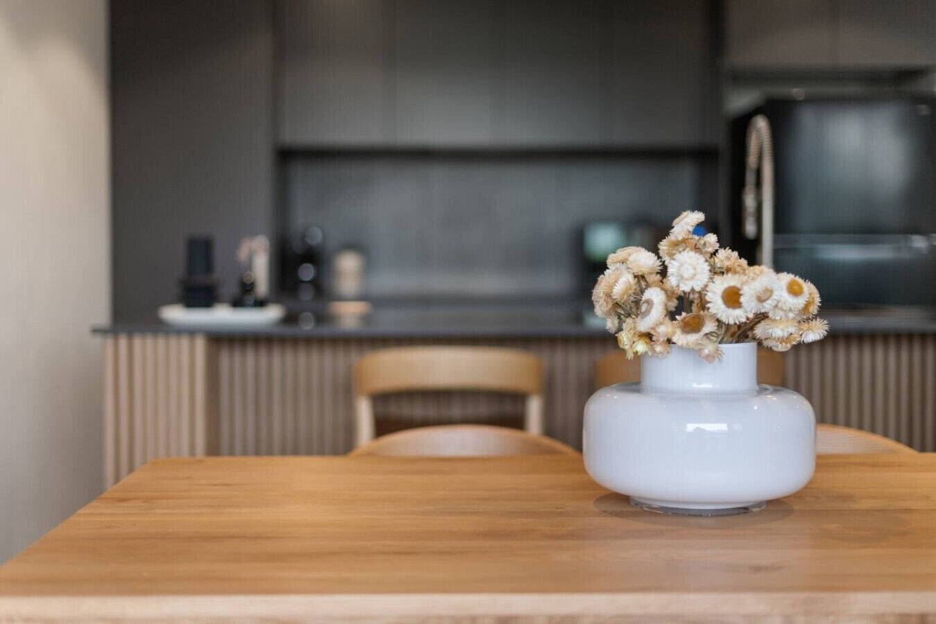 Ruokapöytä, jonka päällä on valkoinen maljakko, jossa on kuivattuja kukkia.