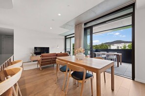 Ein modernes Wohnzimmer mit Essbereich, einer Couch, einem Fernseher und einem großen Fenster mit Blick auf Gebäude und Hügel.