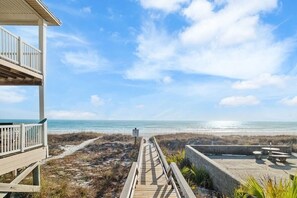 Eine Holzterrasse führt zu einem Strand, der unter einem klaren Himmel liegt.