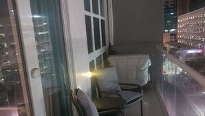 En balkon med to stole og et lille bord, en glasdør og udsigt over bybilledet om natten.