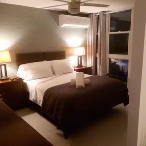 Ein Hotelzimmer mit einem Bett, zwei Nachttischen, einem Deckenventilator und einem Fenster.