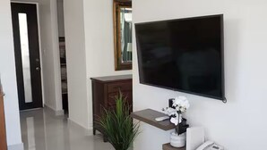 En moderne stue med et fladskærms-tv på væggen, en potteplante, en telefon og et konsolbord.