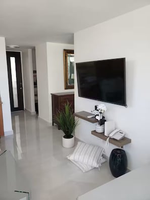 Ein modernes Wohnzimmer mit einem an der Wand befestigten Flachbildfernseher, einer Topfpflanze, einem Telefon und einem Konsolentisch.