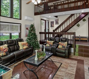 Ein geräumiges Wohnzimmer mit Kamin, Ledersofas, einem Glastisch und einer Treppe.