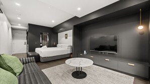 Ein modernes Schlafzimmer mit Bett, Fernseher, Sofa und kleinem Tisch.