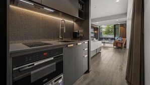 A modern kitchen with a built-in oven, microwave, and convection oven. There is a dining area with a sofa and a table, and a view of the outdoors. - Stylish Studio w/ Generous Balcony, AC & Parking! (Braddon)
