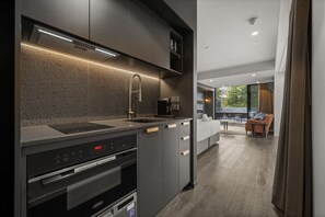 A modern kitchen with a built-in oven, microwave, and convection oven. There is a dining area with a sofa and a table, and a view of the outdoors. - Stylish Studio w/ Generous Balcony, AC & Parking! (Braddon)