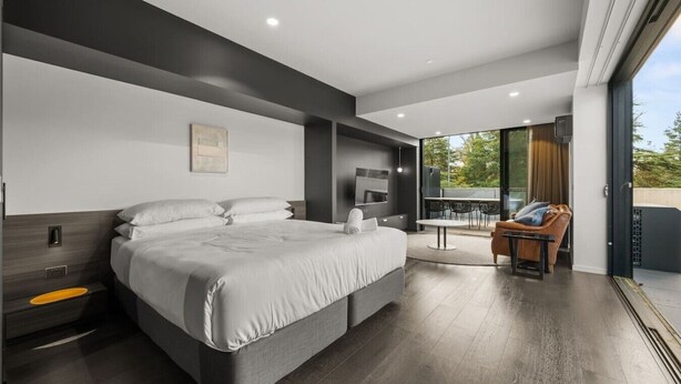 A modern bedroom with a large bed, a TV, and a balcony with outdoor seating. - Stylish Studio w/ Generous Balcony, AC & Parking! (Braddon)