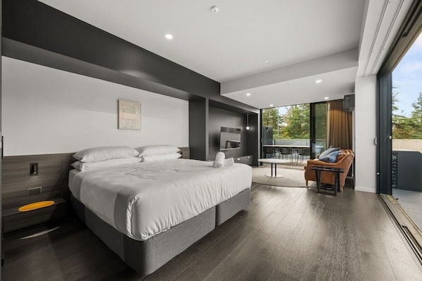 A modern bedroom with a large bed, a TV, and a balcony with outdoor seating. - Stylish Studio w/ Generous Balcony, AC & Parking! (Braddon)