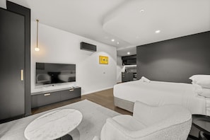 Ein modernes Hotelzimmer mit Fernseher, zwei Betten, einer Essecke und einer Küche im Hintergrund.