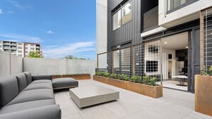 Un espace de vie extérieur moderne comprenant un canapé d’angle, une table basse et des jardinières.
