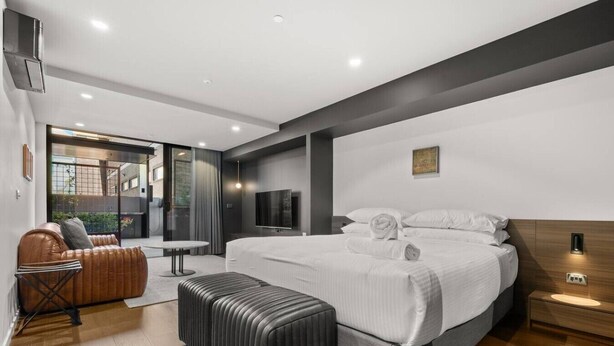 Habitación de hotel moderna con una cama grande, un sofá, una mesita y vistas al exterior.