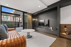 Ein modernes Wohnzimmer mit einer Couch, einem runden Couchtisch, einem flachbildfernseher an der Wand und einer Glastür, die zu einem Außenbereich führt.