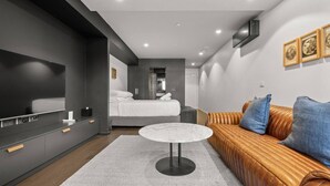 Una habitación de hotel moderna con una cama grande, un sofá, un televisor y una mesita.
